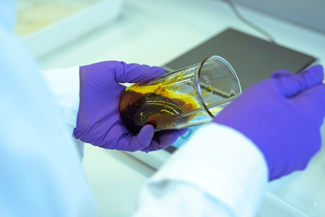 Photographie d'une résine en train d'être mélangée dans un verre doseur. La substance, qui semble semi-liquide, est de couleur ocre jaune.