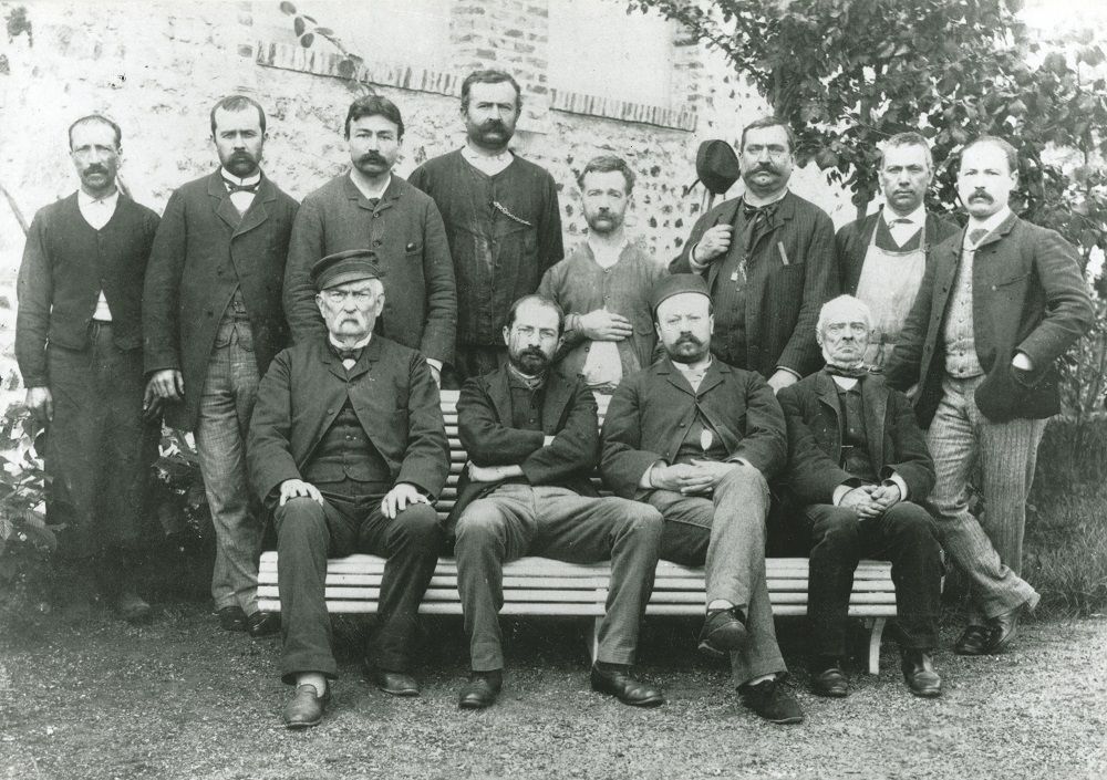 Une photographie de groupe en noir et blanc montre douze hommes posant face à l'objectif. Édouard Michelin (2ème en partant de la gauche, assis) est photographié avec le personnel de l'usine en 1890.