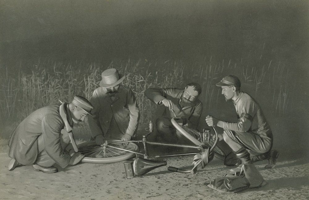 Black and white illustration showing four men on their knees, including Edouard Michelin, repairing a puncture.