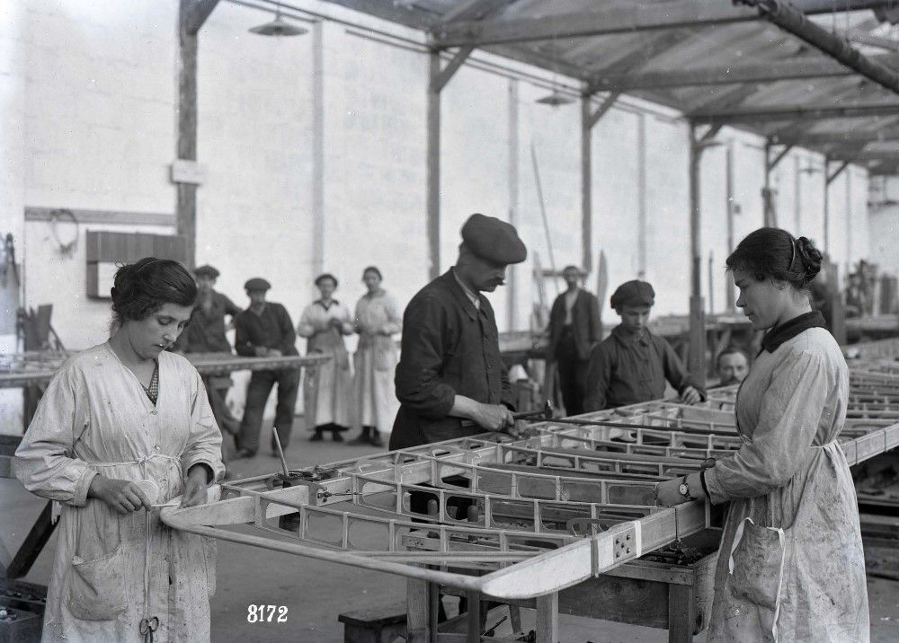 Photographie en noir et blanc d'un atelier de fabrication des Bréguet XIV. L'image montre des hommes et des femmes travaillant à la construction des ailes de l'avion.