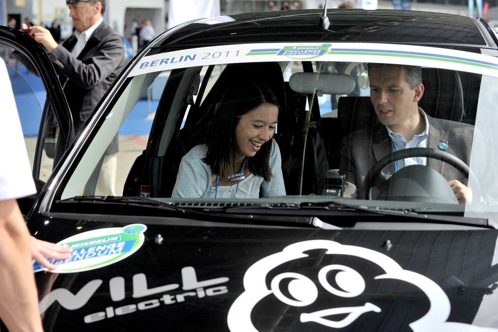 Photograph of two individuals sitting at the front of an electric vehicle and discovering its features.