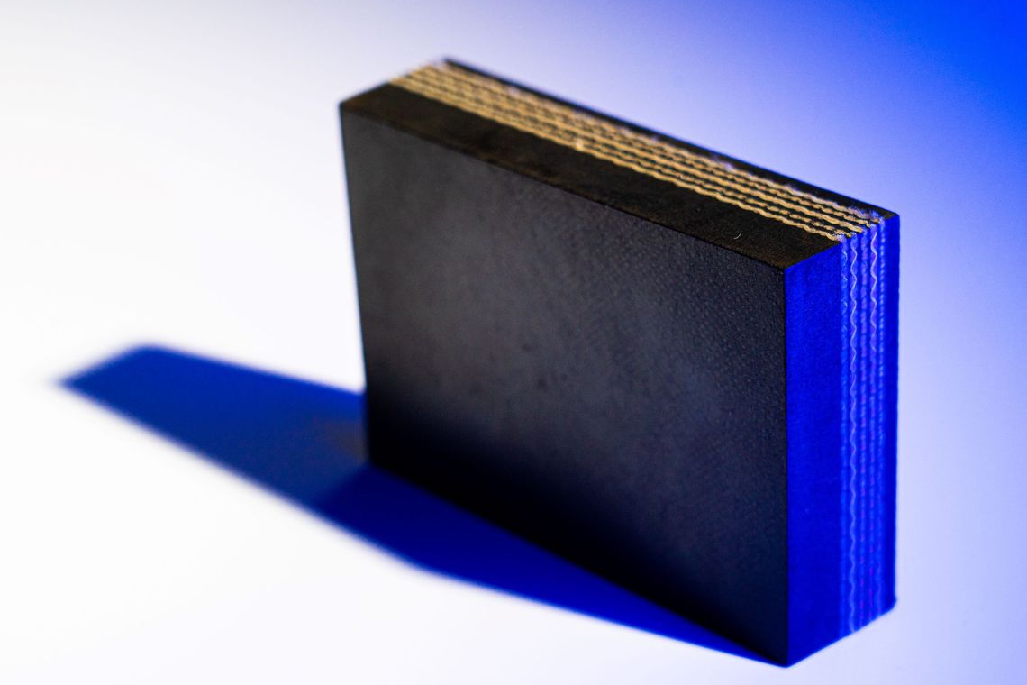Photographie d'un échantillon de bande transporteuse. Il est possible de discerner plusieurs couches superposées de matériaux.