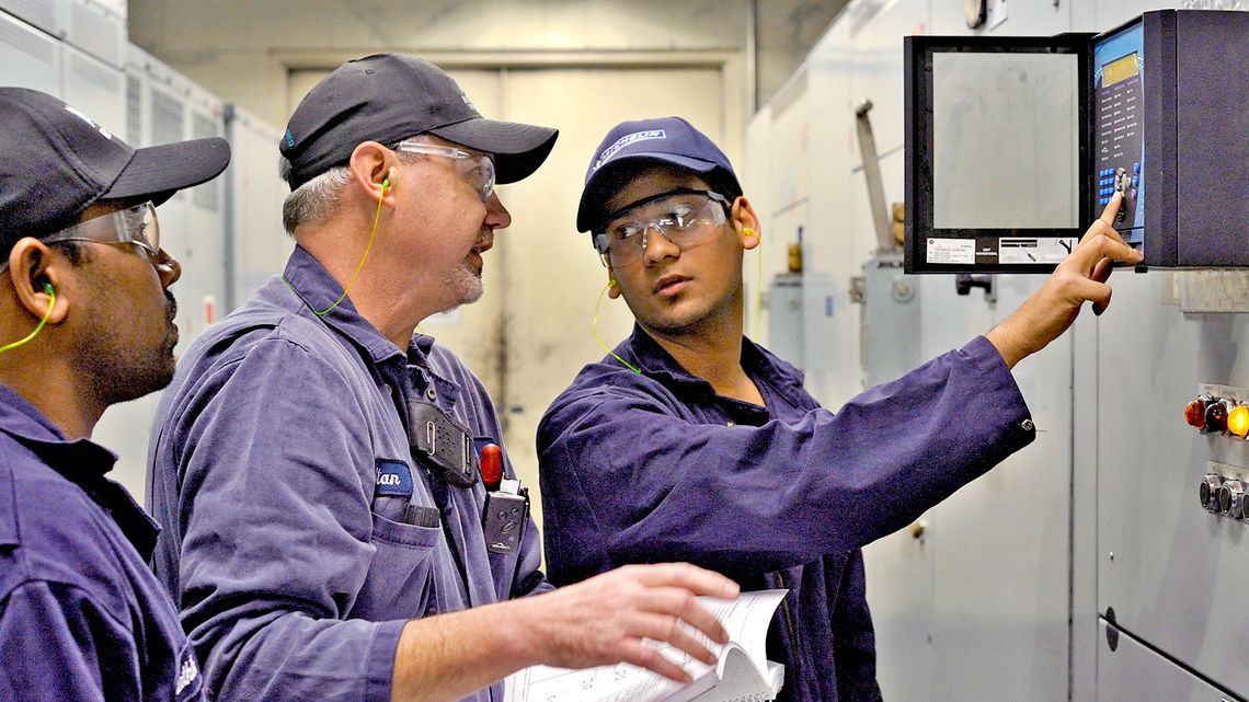An apprentice in a workshop,  operates a machine in the presence of his tutor
