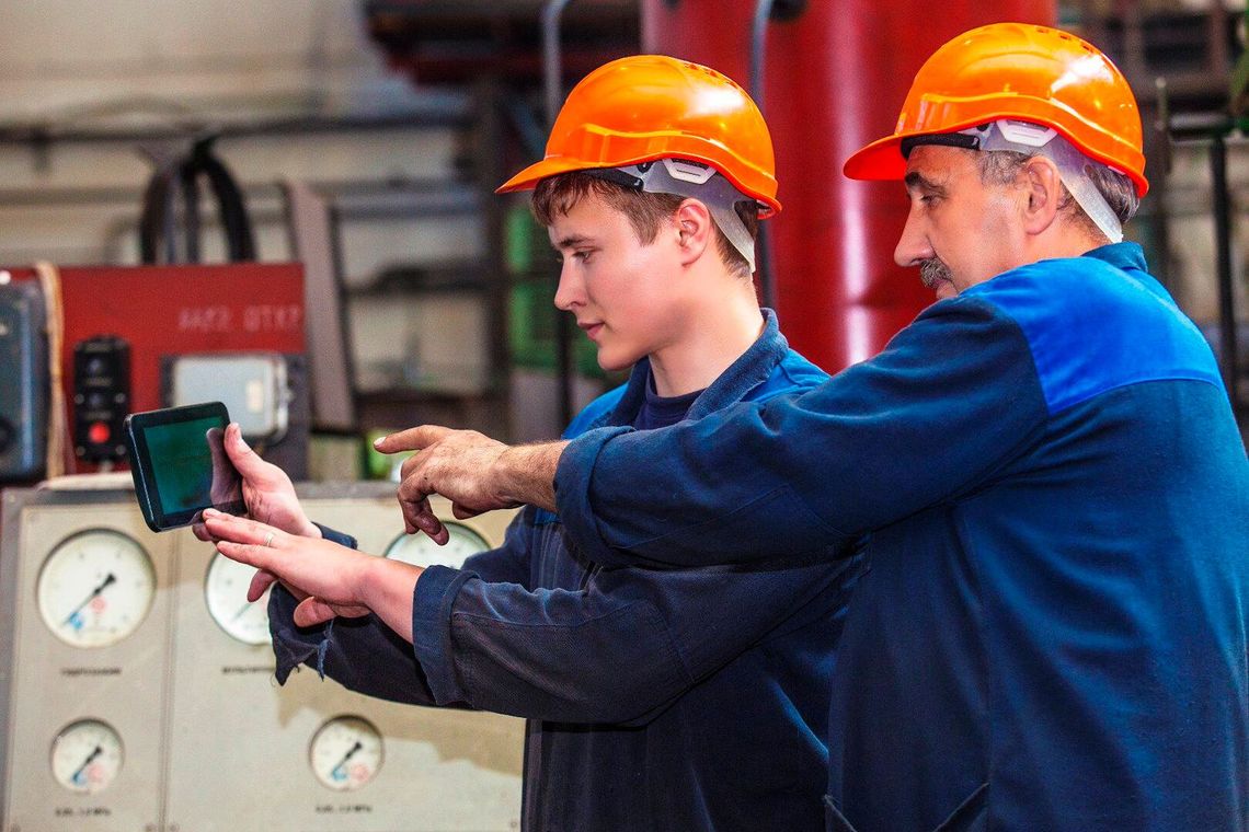 A senior employee trains a young apprentice in a workshop